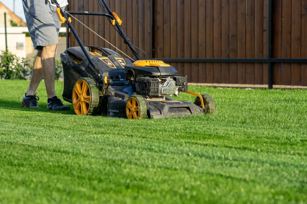 Mann schiebt einen Benzin-Rasenmäher über eine gepflegte grüne Rasenfläche im Garten.