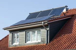 Breite Schleppgaube mit grauer Fassadenverkleidung, Solarthermie-Kollektoren und Photovoltaik-Modulen auf einem roten Ziegeldach.