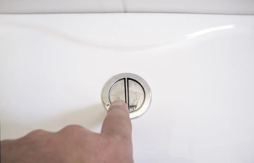Finger drückt die chromfarbene Spültaste für die 2-Mengen-Spülung an einem weißen Spülkasten