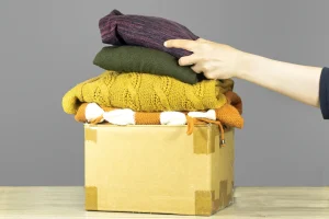 Hand sortiert gebrauchte Kleidung in einen Pappkarton für die Entsorgung von Textilien.