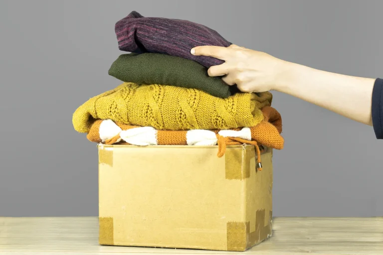 Hand sortiert gebrauchte Kleidung in einen Pappkarton für die Entsorgung von Textilien.