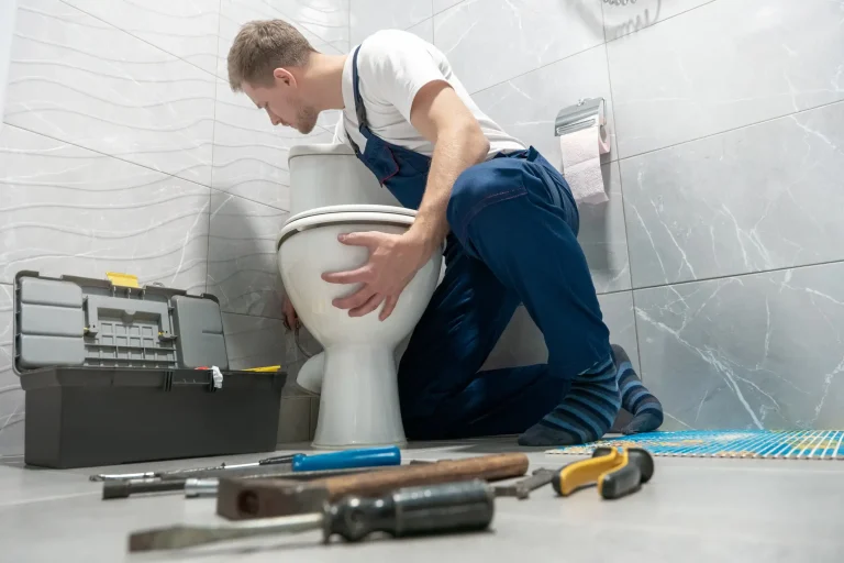 Sanitärinstallateur kniet im Badezimmer und montiert eine weiße Stand-Toilette mit Werkzeug auf dem Boden