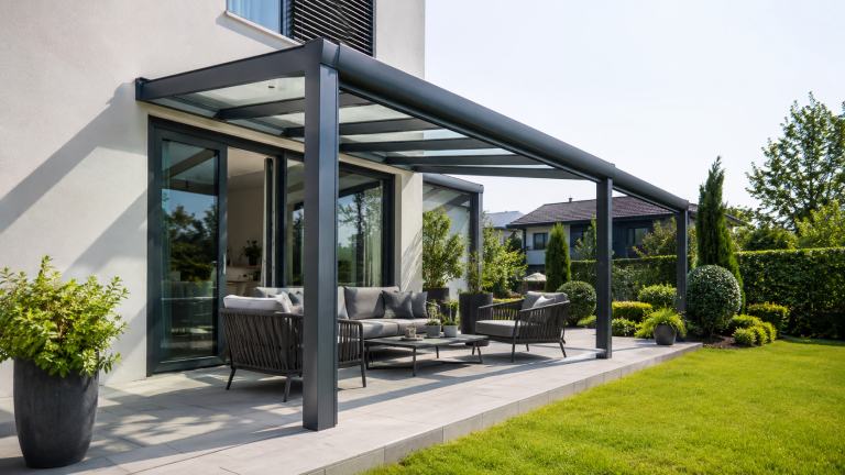 Moderne Terrassenüberdachung aus Aluminium und Glas über einer stilvoll eingerichteten Terrasse mit Sitzmöbeln und Garten.