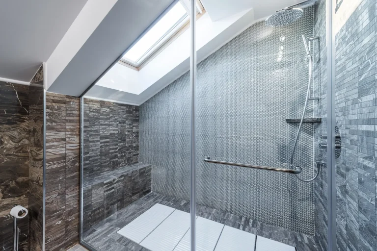 Moderne begehbare Dusche unter einer Dachschräge mit Glaswand, Dachfenster und grauer Mosaik-Fliesenwand.