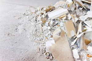 Haufen aus zerbrochenen Gipskartonplatten und Gipsstaub auf einem Betonboden.
