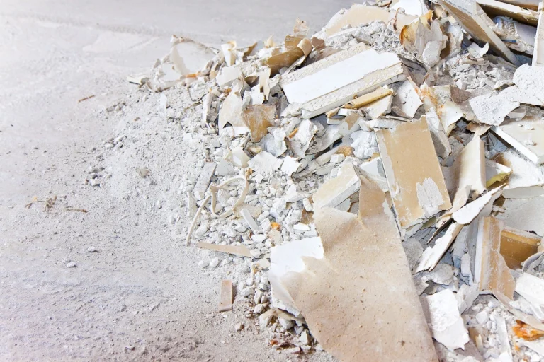 Haufen aus zerbrochenen Gipskartonplatten und Gipsstaub auf einem Betonboden.