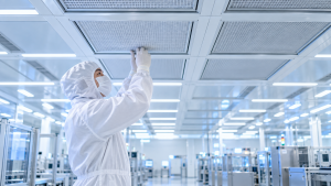 Techniker im weißen Reinraumanzug kontrolliert einen HEPA-Filter in der Decke eines modernen Reinraums.