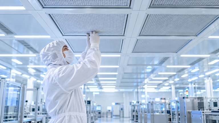 Techniker im weißen Reinraumanzug kontrolliert einen HEPA-Filter in der Decke eines modernen Reinraums.
