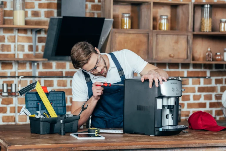 Techniker repariert einen schwarzen Kaffeevollautomaten mit einem Schraubendreher an der Werkbank.