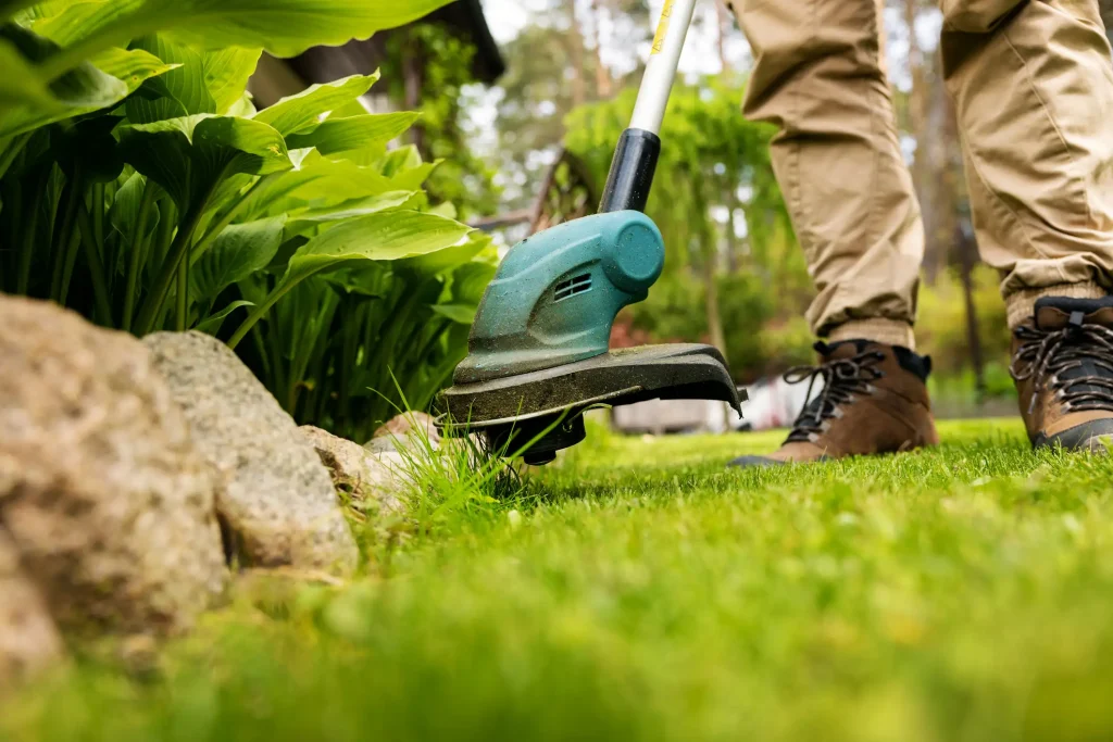 Rasentrimmer schneidet präzise Gras an einer Beeteinfassung aus Steinen im Garten.
