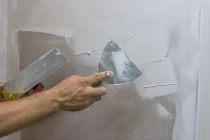 Handwerker trägt weiße Spachtelmasse mit einer Spachtel auf eine Gipskartonwand auf.