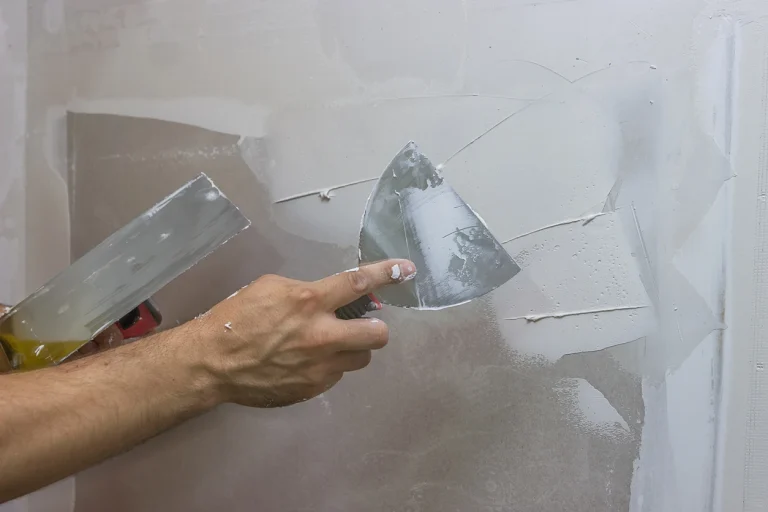 Handwerker trägt weiße Spachtelmasse mit einer Spachtel auf eine Gipskartonwand auf.