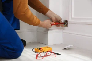 Elektriker montiert eine Unterputz-Steckdose mit einem Schraubendreher an einer weißen Wand.