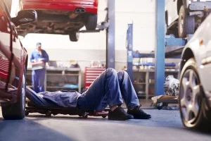Mechaniker liegt unter einem Auto, in einer Werkstatt und repariert den Unterboden.
