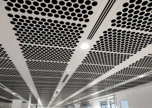 Gelochte Akustikdecke aus Metall mit integrierten LED-Einbauleuchten und Lüftungsschlitzen im Bürogebäude.