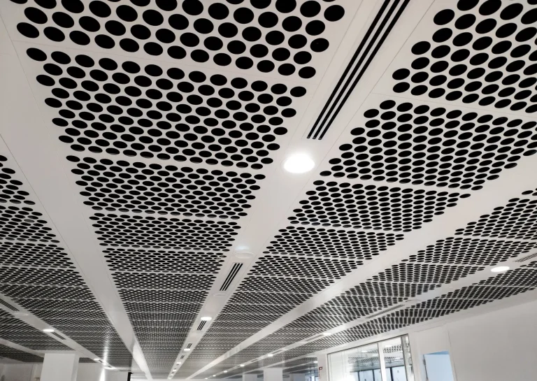 Gelochte Akustikdecke aus Metall mit integrierten LED-Einbauleuchten und Lüftungsschlitzen im Bürogebäude.