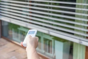 Hand steuert einen elektrischen Rollladen vor dem Fenster mit einer Funkfernbedienung.