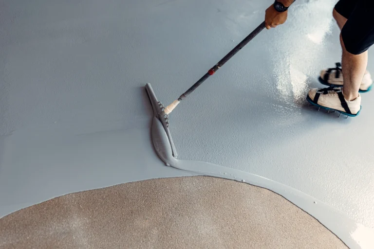 Handwerker verteilt eine graue Epoxidharz-Beschichtung mit einem Rakel auf dem Boden.