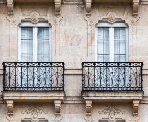 Zwei französische Balkone mit verzierten schwarzen Schmiedeeisengittern an einer historischen Natursteinfassade.