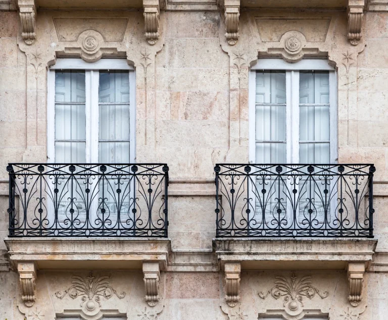 Zwei französische Balkone mit verzierten schwarzen Schmiedeeisengittern an einer historischen Natursteinfassade.