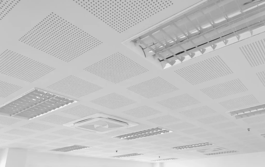 Perforierte Gipskarton-Akustikdecke mit integrierten Rasterleuchten und Deckenkassetten-Klimagerät.