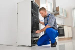 Techniker führt eine Kühlschrank-Reparatur an den Kühl-Verflüssigerlamellen auf der Rückseite durch.
