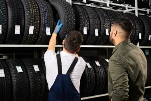 Reifenhändler berät einen Kunden vor einem Regal voller Autoreifen.