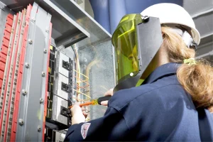 Elektrikerin steht vor einem Sicherungskasten mit Schutzkleidung.