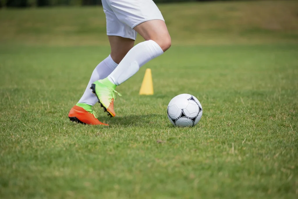 Fußballspieler führt einen Fußball auf einem ebenen, kurz geschnittenen Sportrasen.