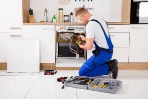 Elektriker überprüft mit einem Multimeter die elektrischen Anschlüsse einer geöffneten Spülmaschine in einer Küche.