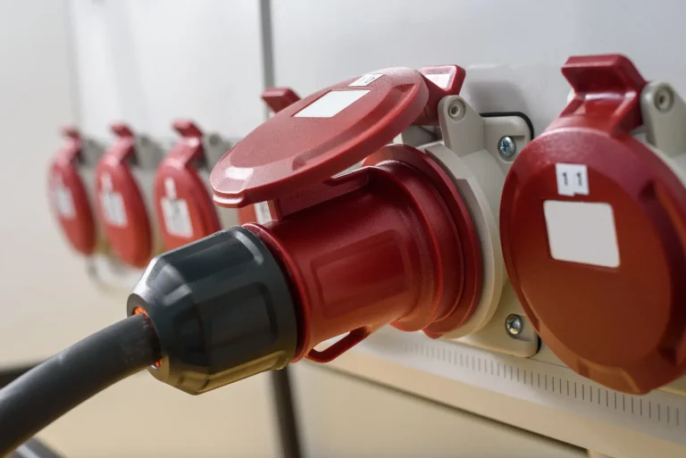 Roter CEE-Starkstromstecker ist in eine CEE-Steckdose an einem Verteilerkasten eingesteckt.