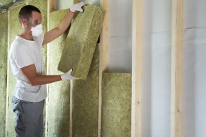 Arbeiter in Schutzkleidung bringt Steinwolle in Holzrahmen an.