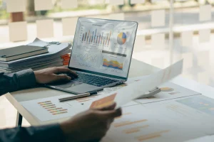 Ein junger Finanzmarktanalyst der im Büro an einem Laptop arbeitet, auf dem einige Statistiken geöffnet sind.