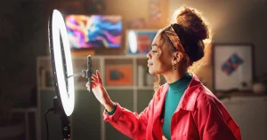 Eine Influencerin richtet ihr Stativ für eine Videoaufnahme aus. Ein Ringlicht steht direkt dahinter.