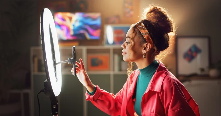 Eine Influencerin richtet ihr Stativ für eine Videoaufnahme aus. Ein Ringlicht steht direkt dahinter.