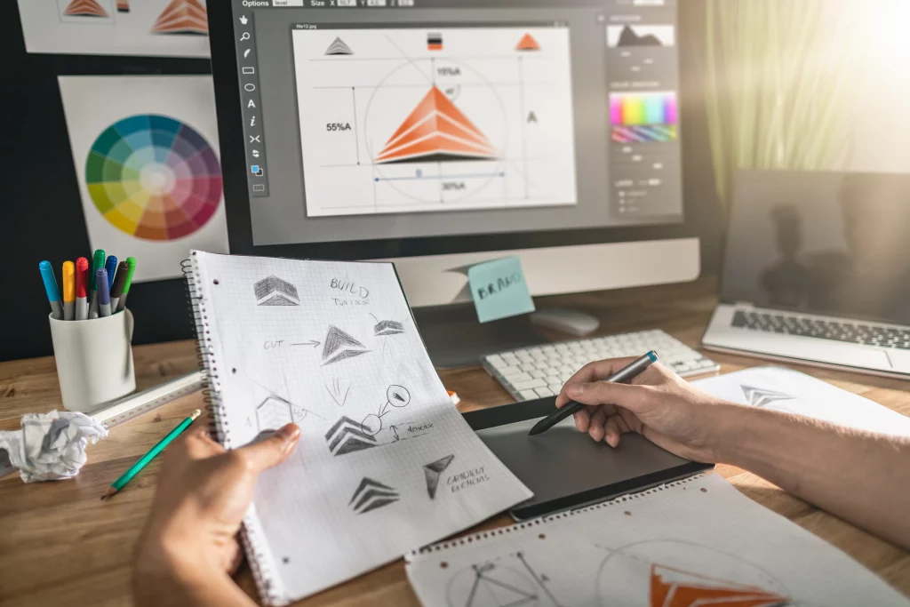 Grafikdesigner bei einer Logoerstellung mit Entwürfen in der linken Hand und PC im Hintergrund