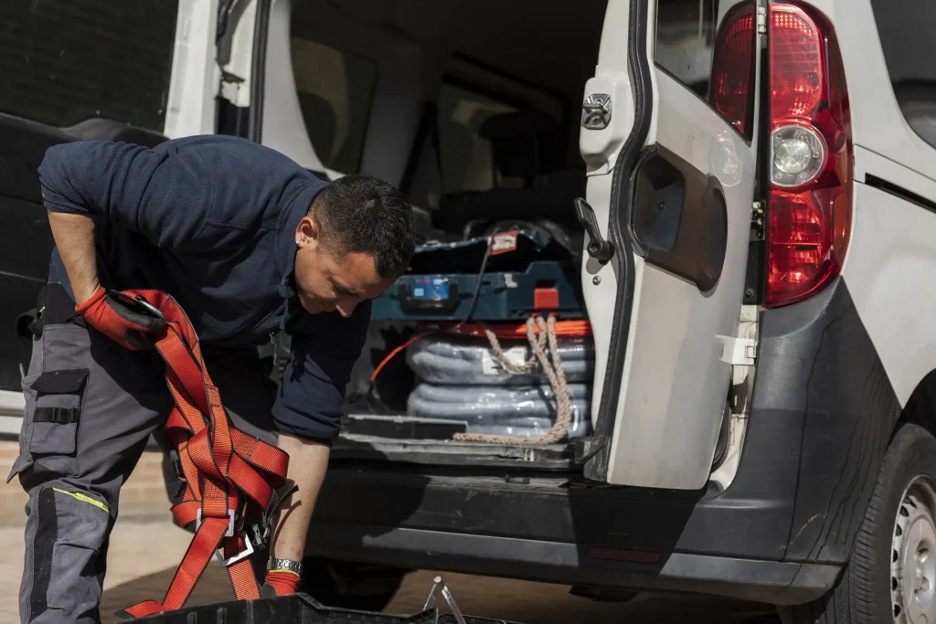 Ein Handwerker In Arbeitskleidung Lädt Werkzeuge Und Ausrüstung Aus Dem Kofferraum Eines Transporters Aus