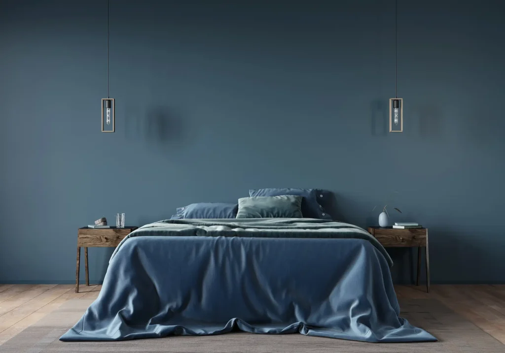 Modern eingerichtetes Schlafzimmer mit hölzernem Boden, einem großen Bett mit blauer Bettwäsche und einer Wand mit glatter, blauer Tapete im Hintergrund.