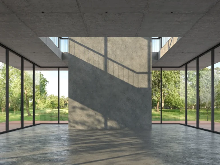 Modernes Gebäude mit großen Glasfronten und Sichtbetonwänden. Der lichtdurchflutete Innenraum kombiniert rohe Betonflächen mit bodentiefen Fenstern und einer offenen Architektur.