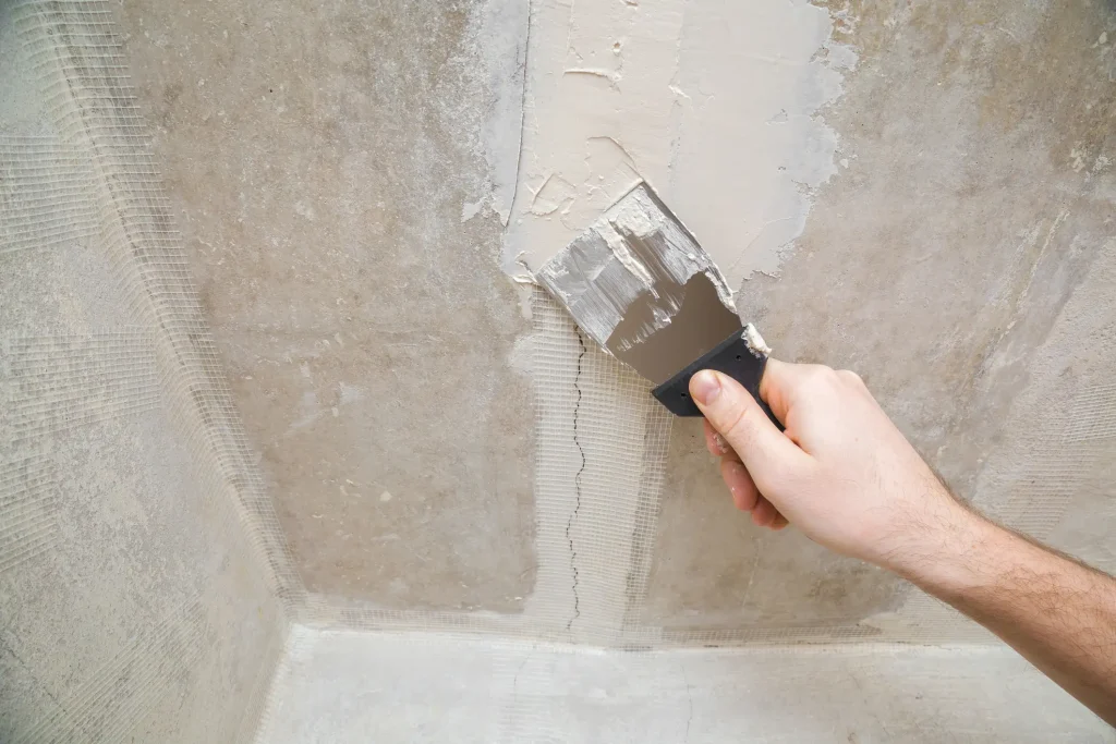 Person trägt Spachtelmasse mit einem Spachtel auf eine Wand auf, um einen Riss mit Armierungsgewebe zu reparieren.