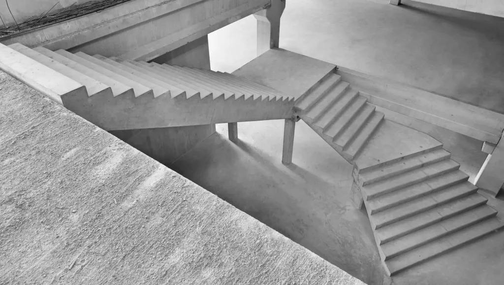 Treppenanlage aus Betonfertigteilen in einem Rohbau. Die Treppenläufe verbinden mehrere Ebenen über Zwischenpodeste. Sichtbare Betonflächen und konstruktive Stützen prägen die industrielle Architektur.