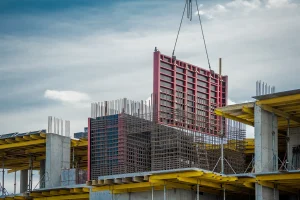Betonschalung auf einer Baustelle im Wohnungsbau: Ein Kran hebt eine große Schalwand, während Bewehrungsstahl und Betonstützen sichtbar sind.