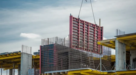 Betonschalung auf einer Baustelle im Wohnungsbau: Ein Kran hebt eine große Schalwand, während Bewehrungsstahl und Betonstützen sichtbar sind.