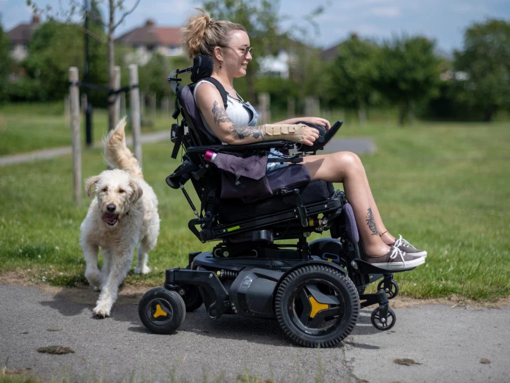 Junge Frau in einem elektrischen Rollstuhl geht mit ihrem Hund spazieren