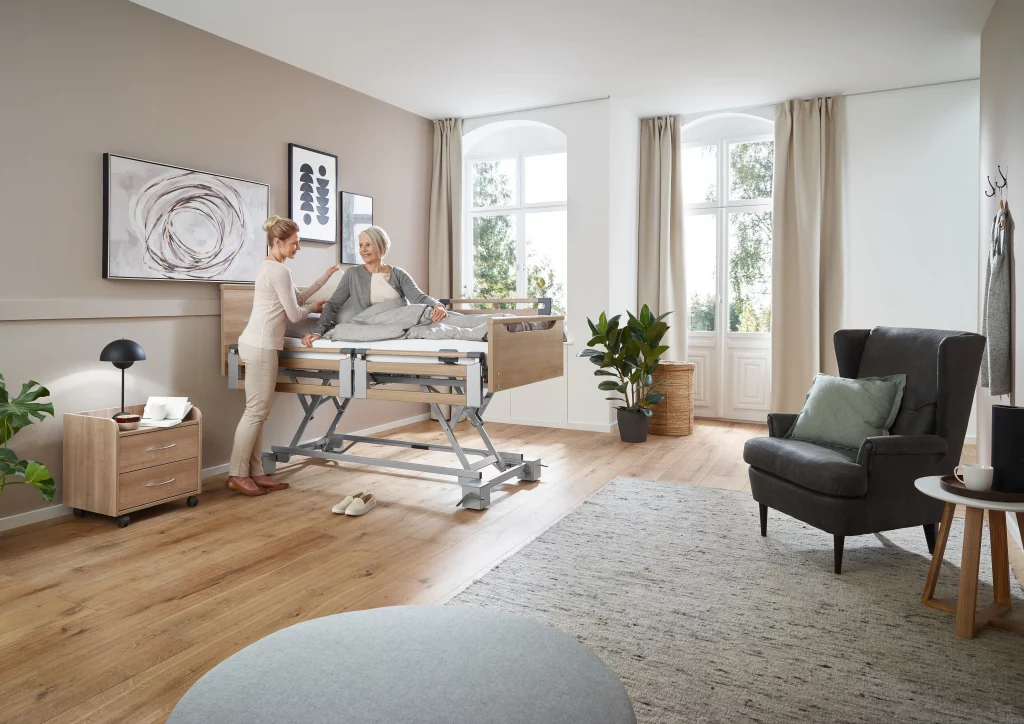 Eine ältere Frau in einem Pflegebett in ihrem Zuhause mit einer Angehörigen