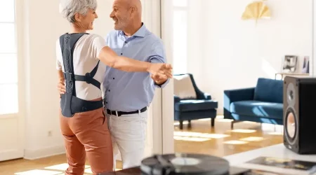 Tanzendes Rentnerpaar, bei der die Frau eine Rückenorthese gegen Osteoporose trägt