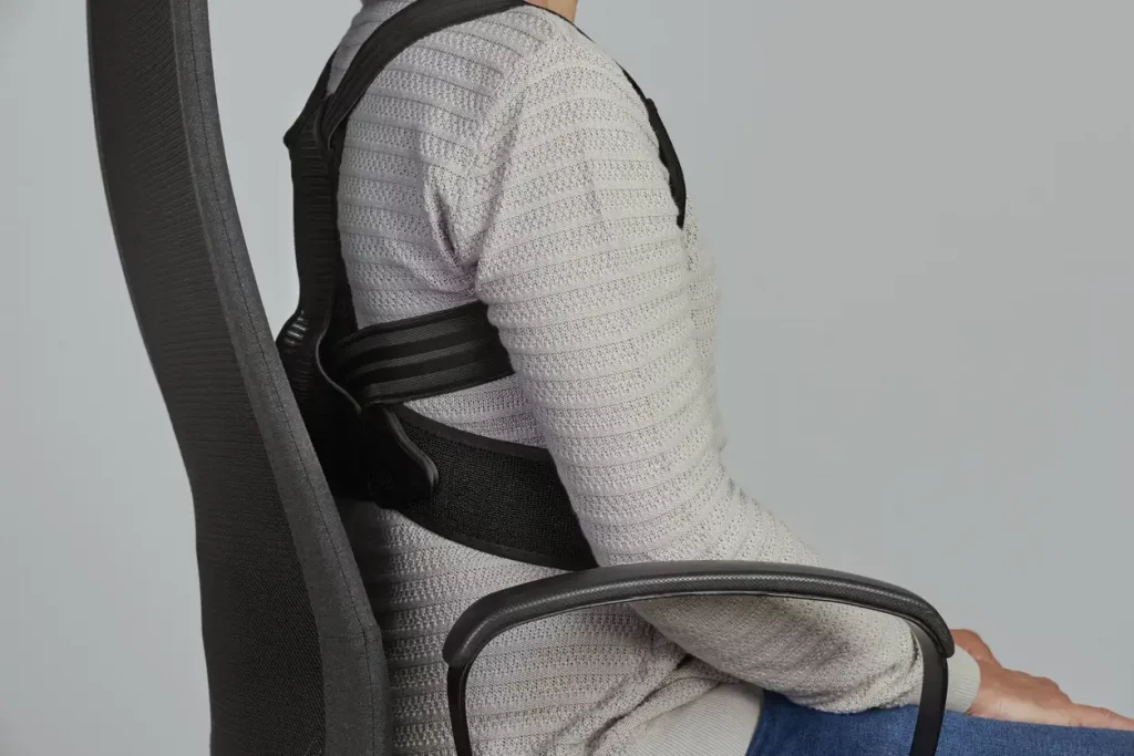 Man sitzt auf einem Bürostuhl mit Rückenorthese zur Unterstützung bei Osteoporose