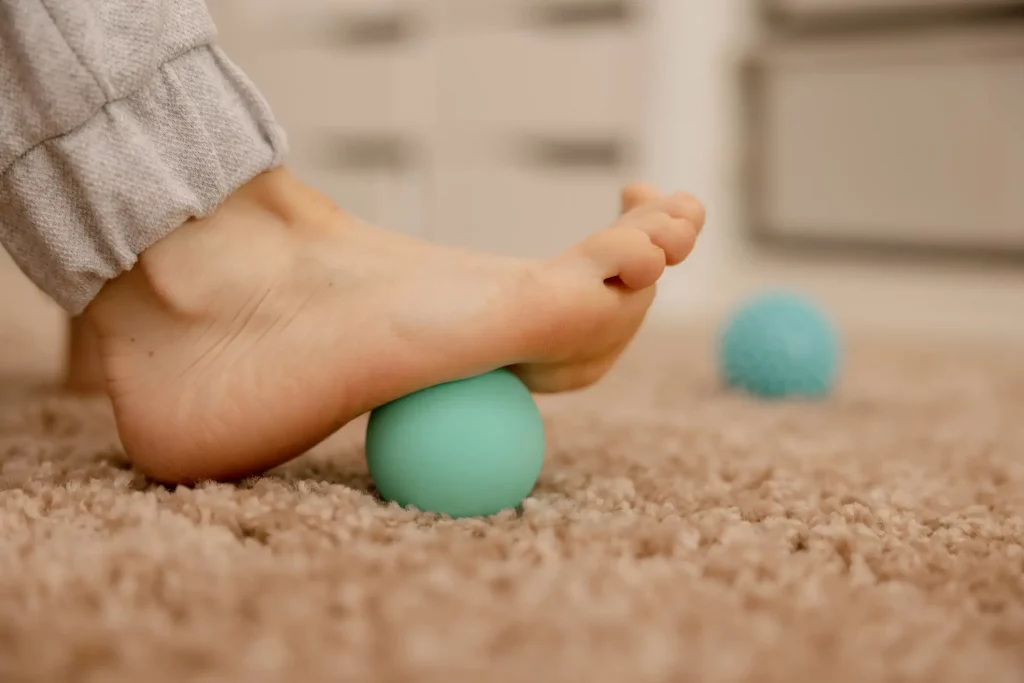 Ein Frauenfuß mach Gymnastikübungen auf einem kleinen turkis farbigen Massageball zur Plattfußkorrektur