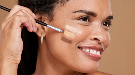 Dunkelhäutige Frau probiert verschiedene Make-Up Töne auf ihrer Haut aus.