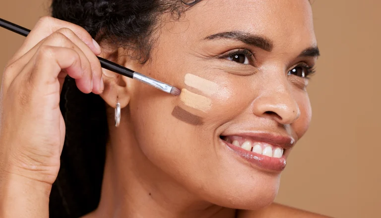 Dunkelhäutige Frau probiert verschiedene Make-Up Töne auf ihrer Haut aus.